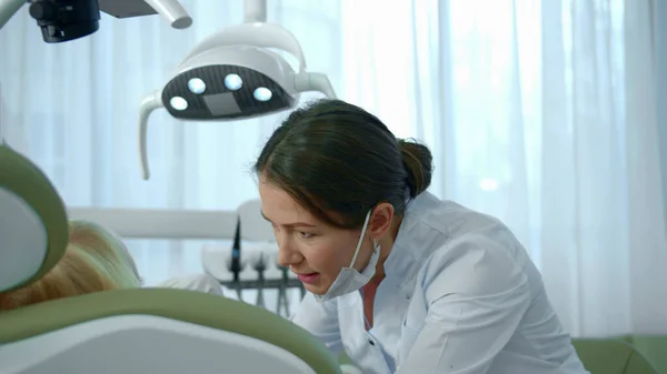 Dentist directs a lamp at the girls mouth and looks at her teeth.