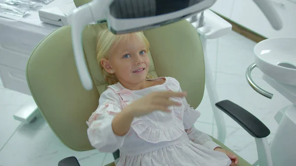 Kleines Mädchen sitzt im Zahnarztstuhl, berührt eine Lampe — Stockfoto