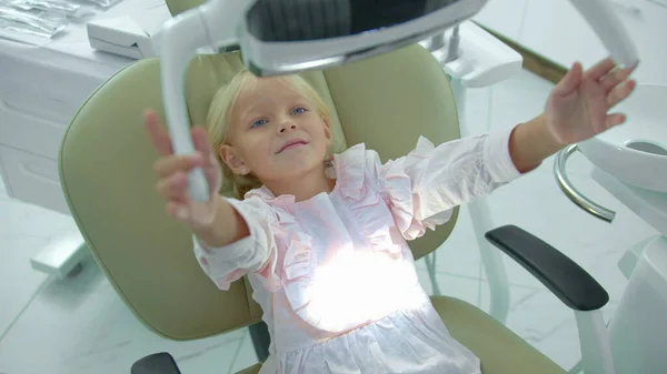 Menina liga uma lâmpada sentada em uma cadeira de dentista — Fotografia de Stock