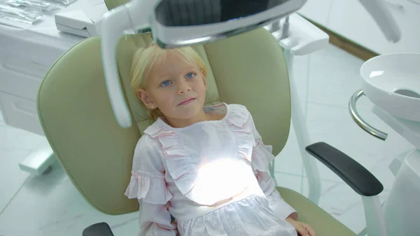 Meisje zit in tandartsstoel, zet uit en op de lamp — Stockfoto