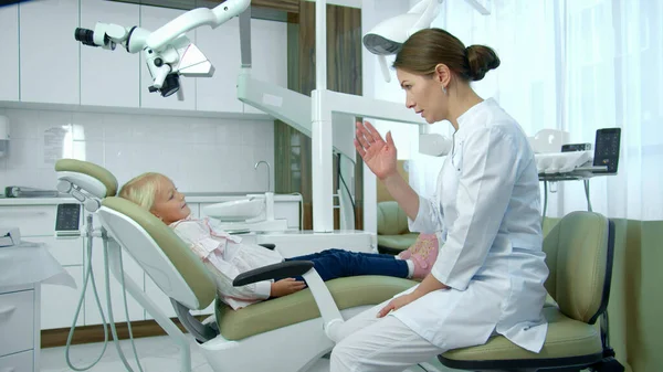 Zahnärztin spricht mit kleinem Mädchen in Klinik. — Stockfoto