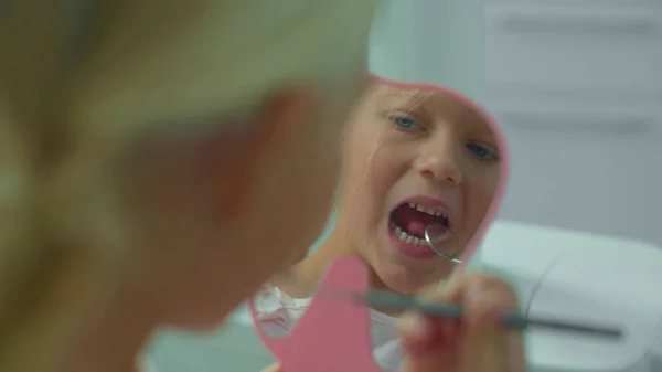 Маленькая девочка смотрит на свои зубы в зеркало . — стоковое фото