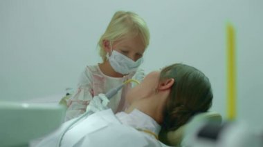 Kız doktorun ağzına tükürük püskürtücü koyuyor.