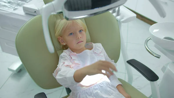 Menina bonita senta-se na cadeira do dentista, desliga uma lâmpada — Fotografia de Stock