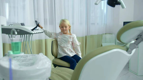 Mała dziewczynka podnosi krzesło dentystyczne w klinice — Zdjęcie stockowe