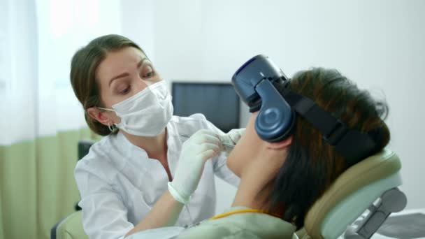 Diş hekimi çalışıyor, hastası sanal gerçeklik gözlüğü takıyor. — Stok video