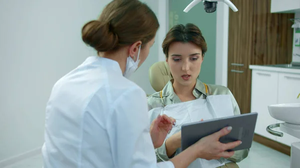 Dentista fala com paciente e mostra-lhe algo no tablet — Fotografia de Stock