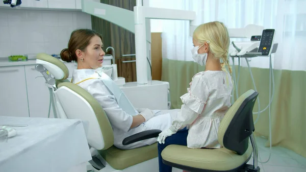 Dentista senta-se na cadeira do paciente e conversa com menina — Fotografia de Stock