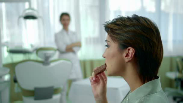 Молодая девушка ест шоколад, стоматолог шокирован — стоковое видео