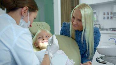 Diş hekimi tıbbi bir yöntem gösterir, bir kız güler.