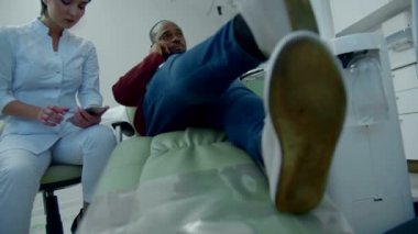 Doktor telefonla konuşuyor, hasta müzik dinliyor.