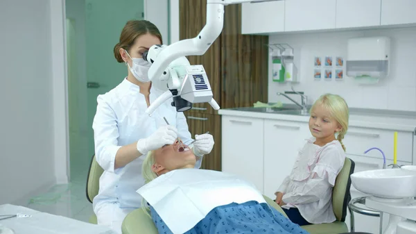 Dentista olha para os dentes das mulheres com um equipamento odontológico — Fotografia de Stock