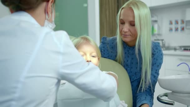 Dentista sujeta un pañal en una chica y toma un taladro médico — Vídeo de stock