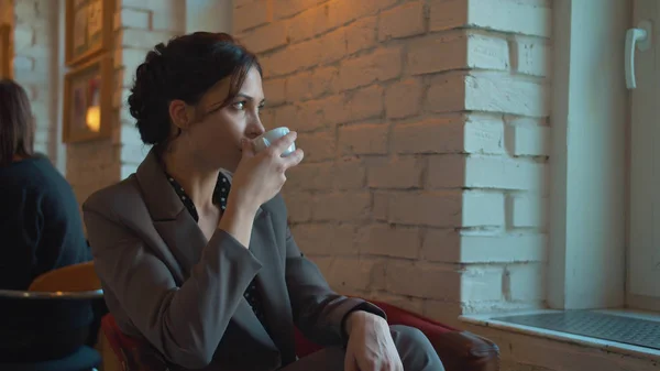 Bayan kahve içer ve pencereden dışarı bakar.