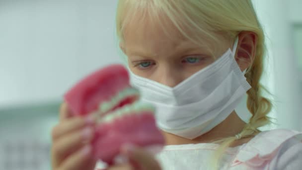 마스크를 쓴 소녀가 의료용 턱 본을보고 있습니다.. — 비디오