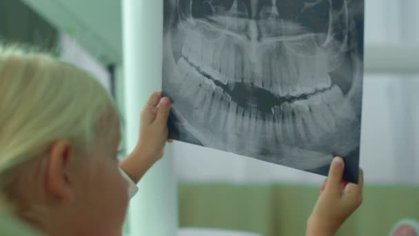 Chica está mirando la radiografía de sus dientes en el gabinete . — Vídeos de Stock