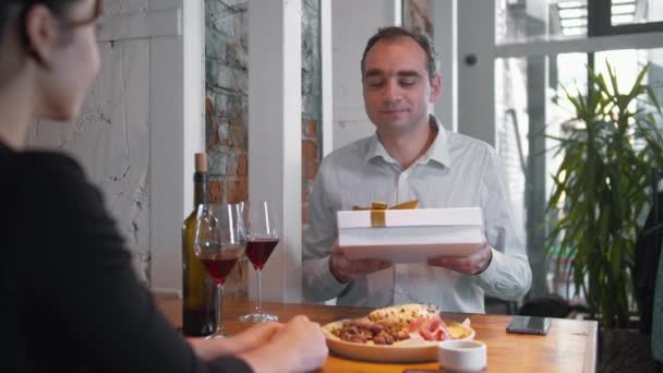 Cena romántica, hombre da un regalo a su mujer con una sonrisa — Vídeo de stock