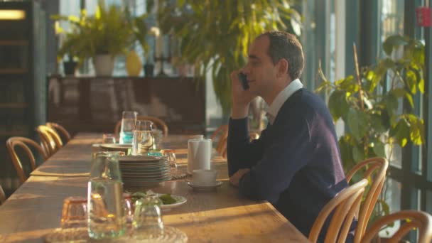Вид сбоку, мужчина разговаривает по телефону в кафе — стоковое видео