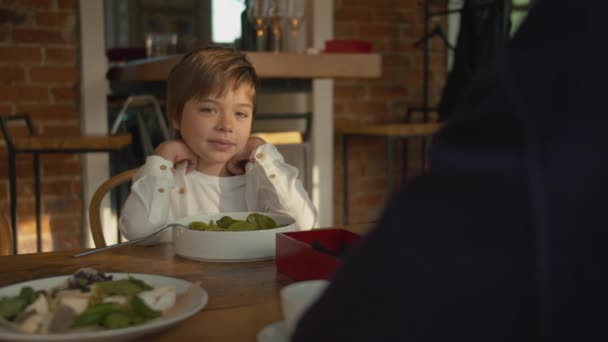 Niño pequeño se sienta en una mesa de madera en un café — Vídeo de stock