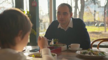 Baba, öğle yemeğinde oğluyla konuşuyor.