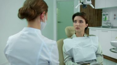 Maskeli diş hekimi bir kızla konuşuyor. 