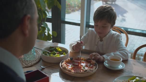 Junge schneidet mit Messer Pizza, Vater hilft ihm — Stockvideo