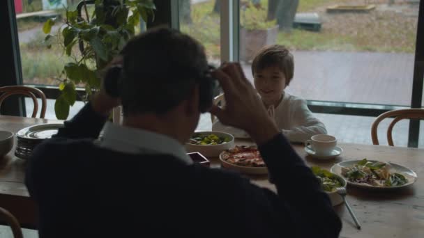 Ojciec zakłada okulary wirtualnej rzeczywistości podczas lunchu z synem — Wideo stockowe