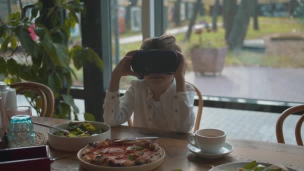 Jongen kijkt rond in virtual reality bril tijdens de lunch — Stockvideo