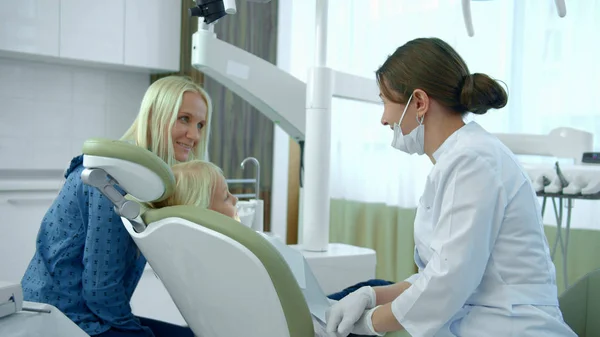 Ragazzina seduta su una sedia dentale, sua madre parla con un medico — Foto Stock