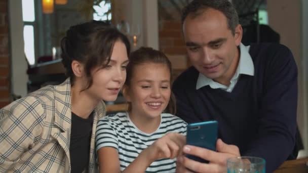 Os pais e a filha estão vendo fotos no telefone ao almoço — Vídeo de Stock