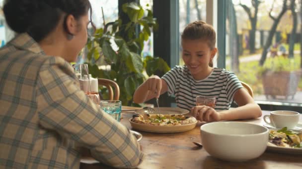 Chica corta una pizza en el almuerzo con madre — Vídeos de Stock