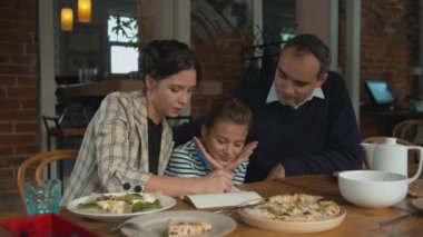 Ebeveynler ve kızları deftere birlikte bir şeyler yazıyorlar.