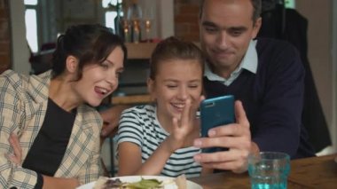 Ebeveynler ve kızları telefona bakar ve fotoğraflara güler. 
