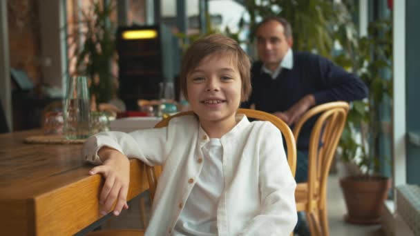 Niño, siéntate en la silla, mira la cámara y sonríe. — Vídeos de Stock