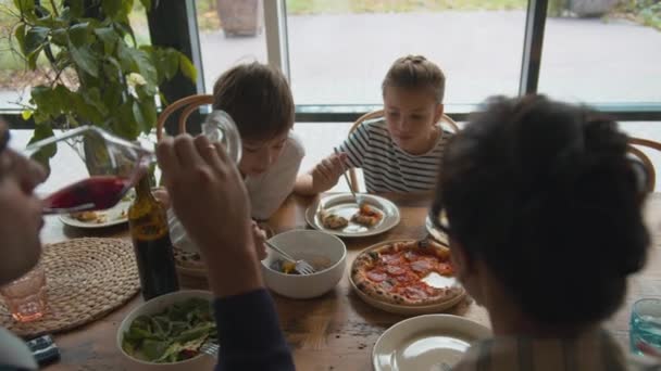 Chico pone tenedor en un plato con comida, chica come pizza, padre bebe vino en un café — Vídeo de stock