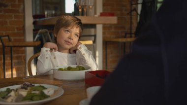 Küçük çocuk bir kafedeki ahşap masada oturuyor. 