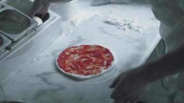 Şef pizza hamuruna domates ezmesi ve peynir sürer.