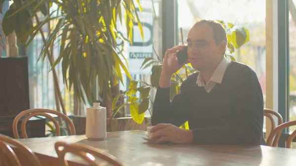 El hombre se sienta en la cafetería y habla por teléfono —  Fotos de Stock