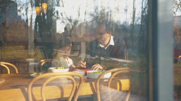 Outside the window, father explain to his son how to write
