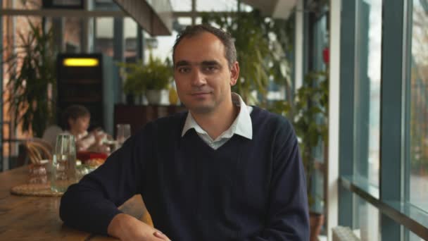 Homme assis sur une chaise dans un café et regarder la caméra avec le sourire — Video