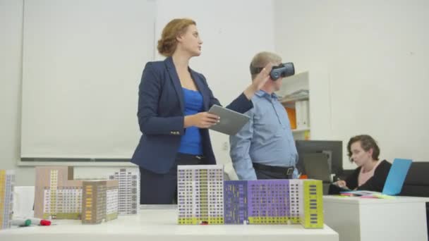 Жінка з планшетом в руках показує щось колезі у віртуальних окулярах в офісі — стокове відео