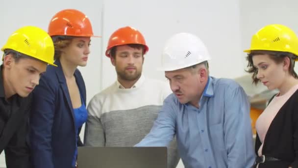 Man in helmet explains something to his colleagues with laptop — ストック動画