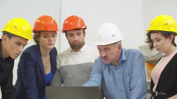 Compagni di lavoro in casco stand e ascoltare l'uomo parlante, che mostra qualcosa sul computer portatile — Video Stock