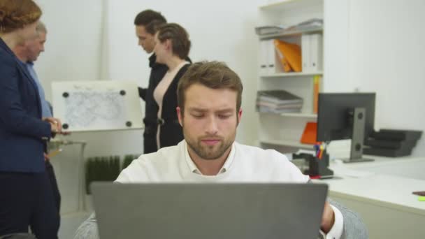 Man die werkt op de laptop, zijn collega 's bespreken de regeling van appartement — Stockvideo