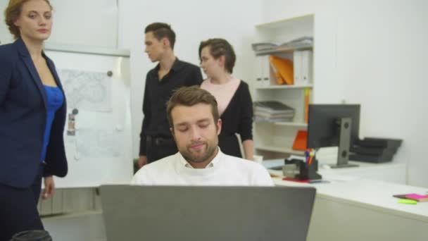 El joven trabaja y sus colegas viven la oficina y le dan una bofetada en el hombro — Vídeo de stock