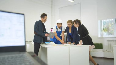 Adam tablette bir grup mühendise şemayı gösteriyor, ev projesini tartışıyorlar.