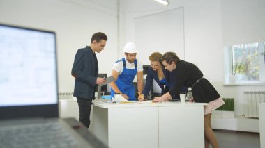 Üniformalı inşaatçı ve bir grup mühendis ev planlarını tartışıyor