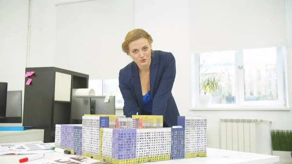 Mujer de pie al lado de la maqueta de casas y explica algo sobre la construcción en cámara — Foto de Stock