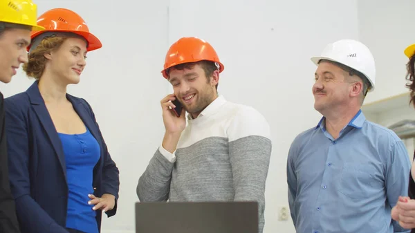 Mężczyzna w kasku rozmawia przez telefon podczas spotkania z architektami — Zdjęcie stockowe