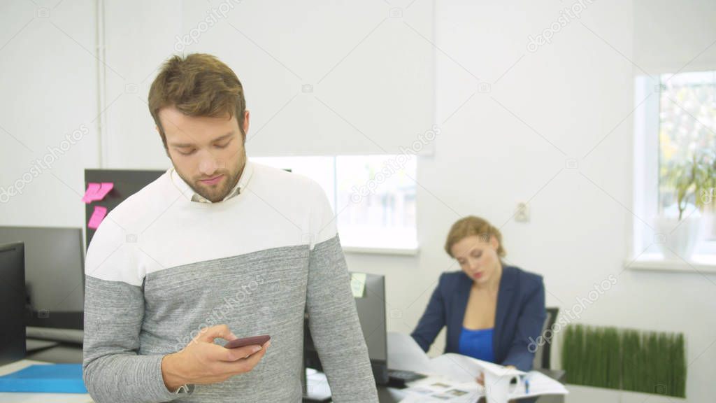 Builder types something on phone, woman behind him looks on schemes of houses